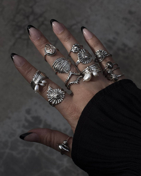 Hand wearing multiple silver rings on a dark textured background