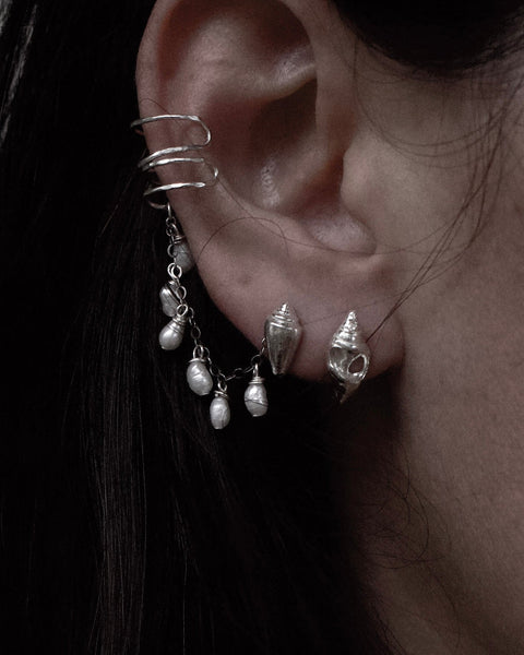 Close-up of an ear with a silver spiral earring and shell-shaped earrings.