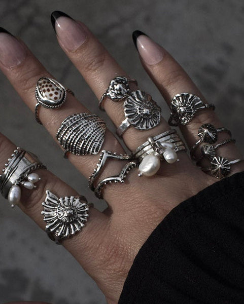 Hand wearing multiple silver rings on a dark textured background. Lost Wax Casted and one of a kind opihi and shell rings made in hawaii